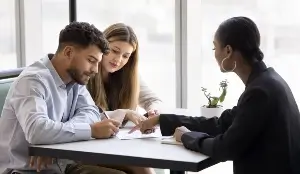 Mortgage lender pointing at a paper agreement for a couple of clients signing mortgage loan, real estate property buying