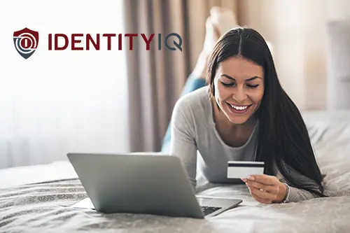 Woman smiling while laying on a bed with her bank card and laptop