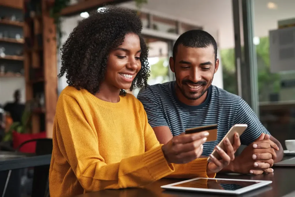 A couple working on a phone and tablet with a bank card while smiling