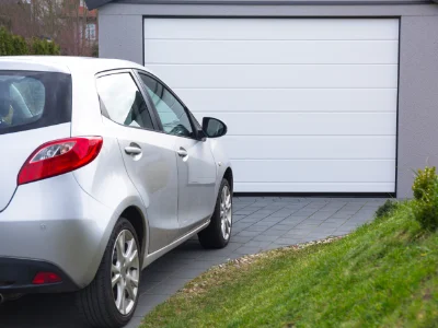 A silver hatchback parked on a paved driveway in front of a modern closed white garage door.